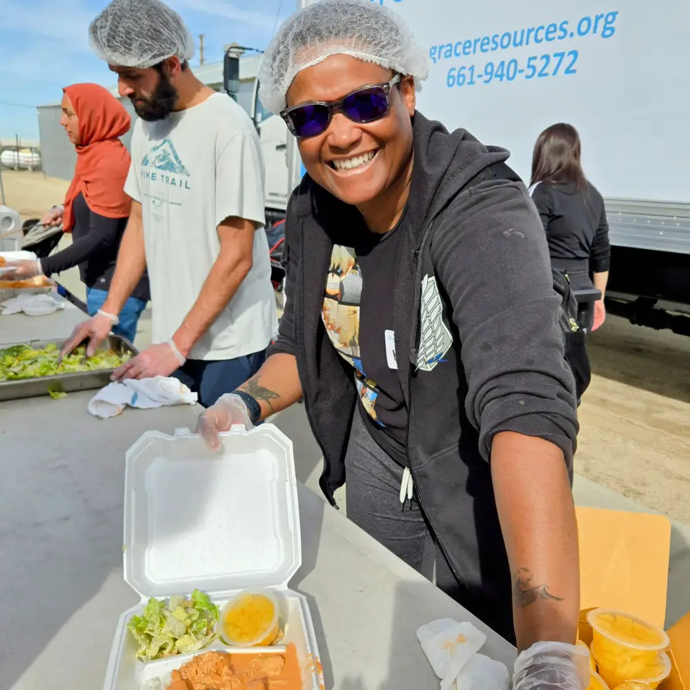 serives page webp webp Individuals prepare and serve meals, featuring trays of salad, chicken, and sides, at a community outreach event.